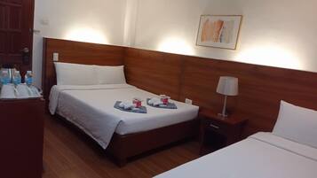 Een hotelkamer met twee bedden, houten hoofdborden, wit beddengoed, een nachtkastje met een lamp en een schilderij aan de muur.