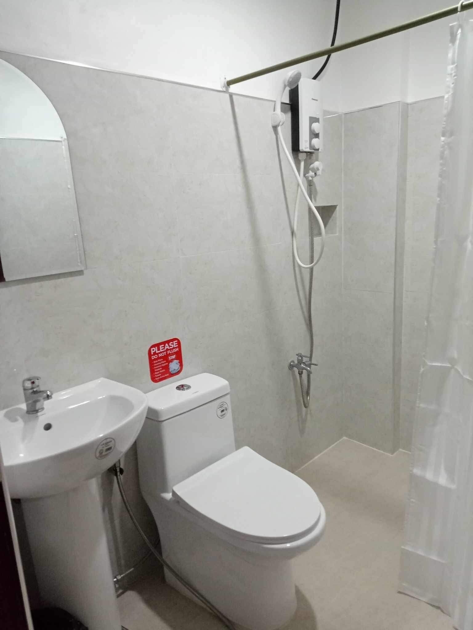 Un baño con lavamanos, inodoro y ducha. Hay un cartel en el inodoro.