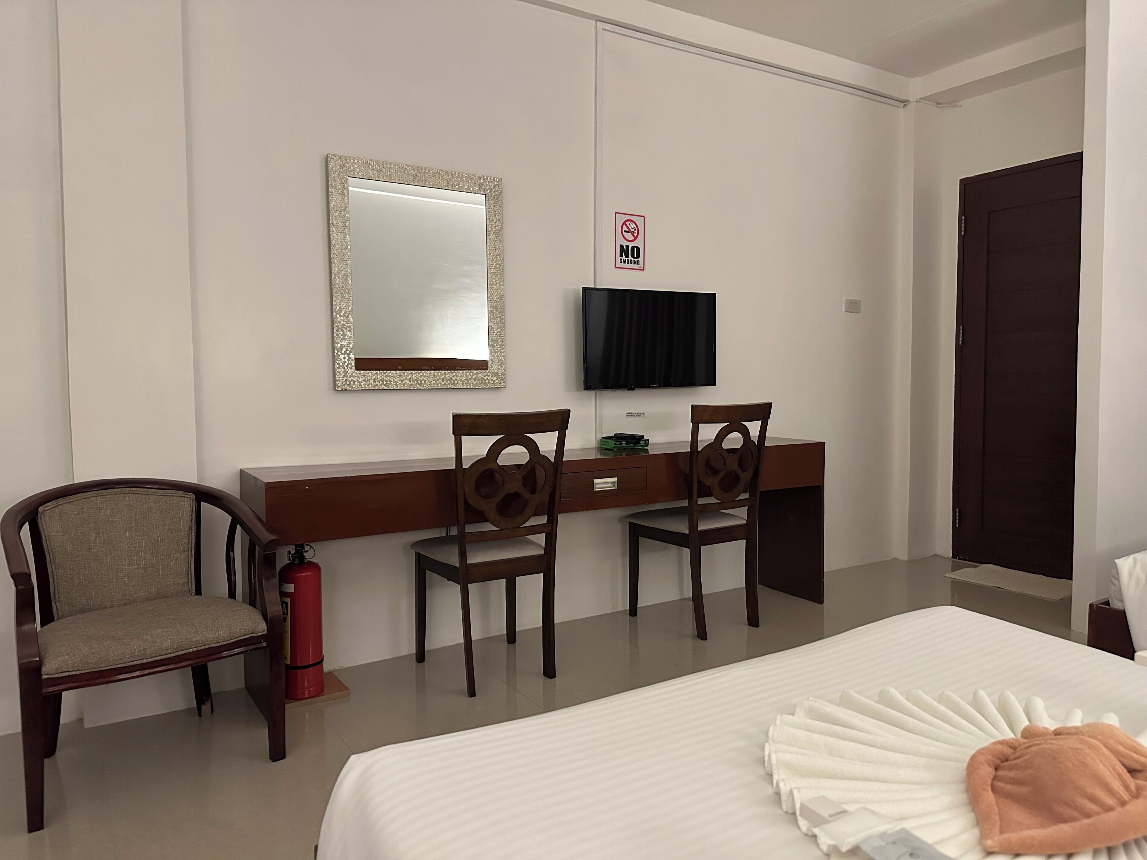 Habitación de hotel con una cama, dos sillas, un escritorio, un televisor y un cartel de 'No Fumar'.
