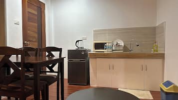 A compact kitchen with a refrigerator, microwave, and sink. There is a dining table with chairs and a small round table.