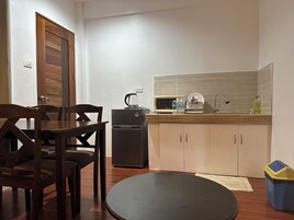 Cocina compacta con refrigerador, microondas y lavamanos. Hay una mesa de comedor con sillas y una pequeña mesa redonda.