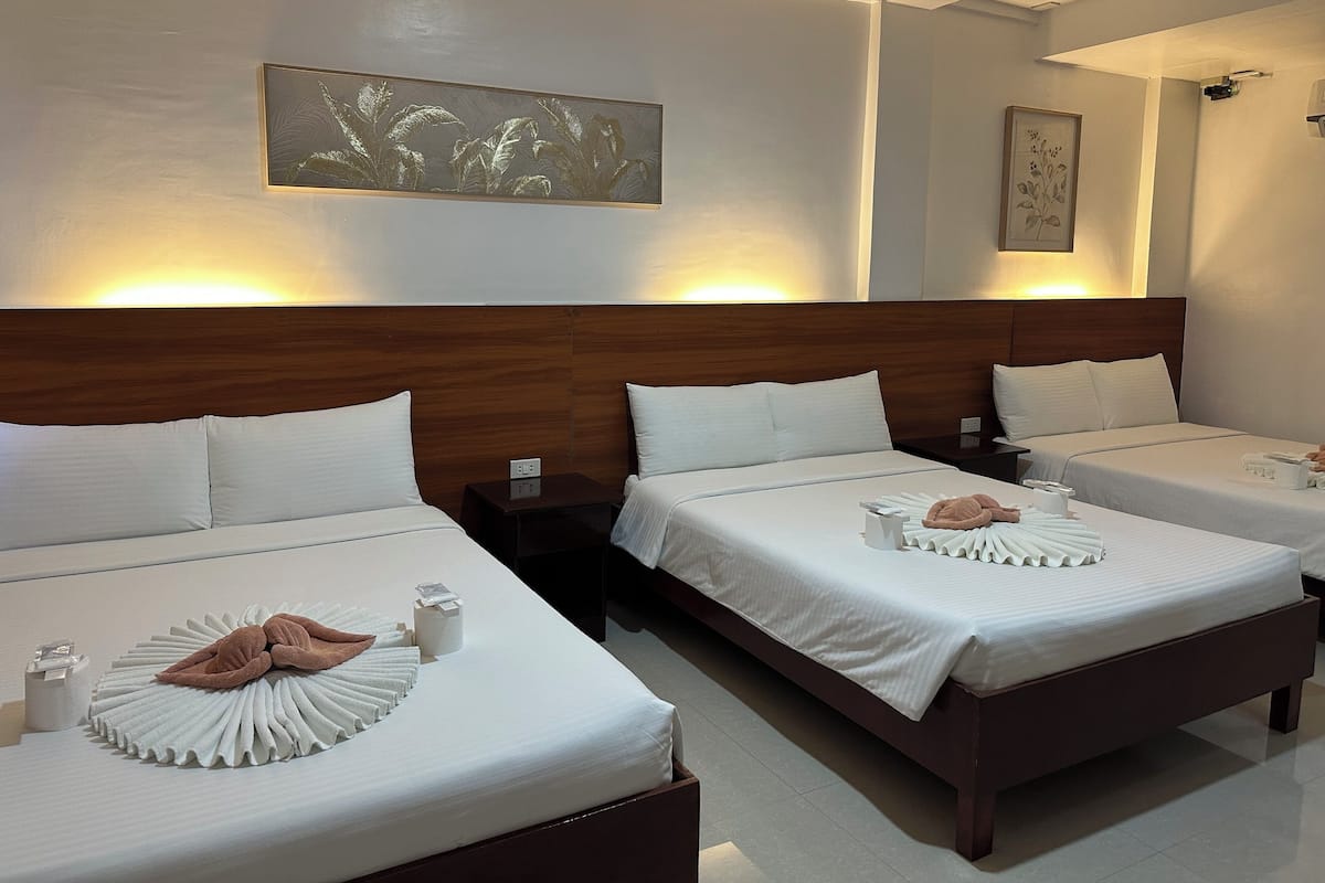 Ein Hotelzimmer mit zwei Betten, jeweils mit weißer Bettwäsche und einem ordentlich gefalteten Handtuch. An den Wänden sind Lampen angebracht und über den Betten hängt ein gerahmtes Kunstwerk.
