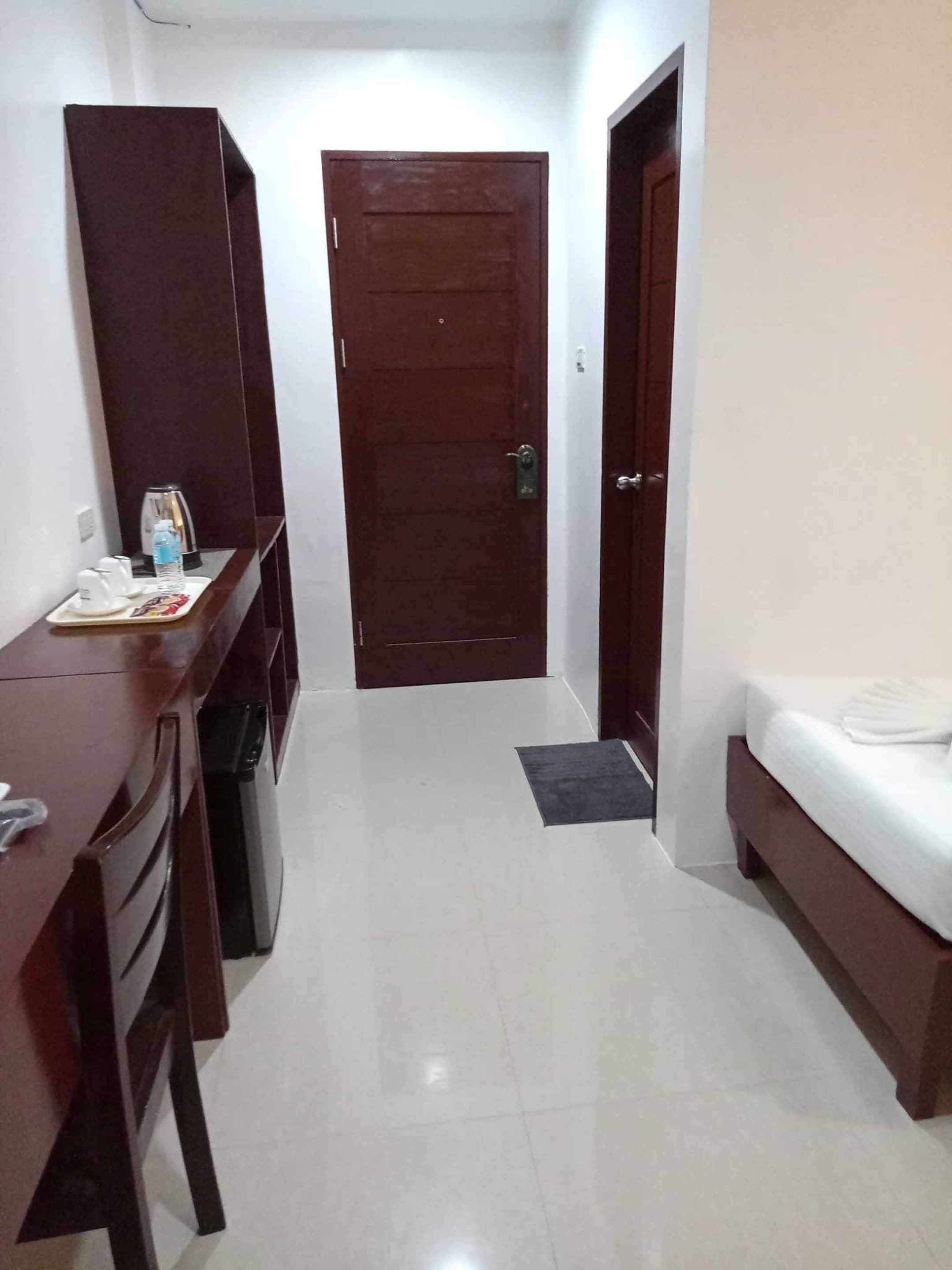 A hotel room with a bed, a desk with a chair, a wardrobe, and a door.