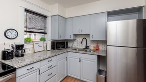 A modern kitchen with white cabinets, a stainless steel refrigerator, a microwave, and a coffee maker. - Near Downtown ~ 2BDR & Fun Backyard ~ Pet Friendly (Des Moines)