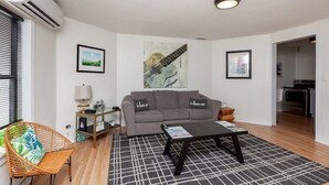 A living room with a grey sofa, a coffee table, a wicker chair, and a black and white rug. - Near Downtown ~ 2BDR & Fun Backyard ~ Pet Friendly (Des Moines)