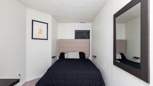 A bedroom with a bed, a large mirror, a framed picture on the wall, and a window with an air conditioning unit. - Near Downtown ~ 2BDR & Fun Backyard ~ Pet Friendly (Des Moines)