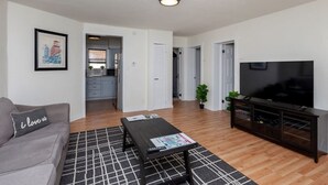 A modern living room with a grey sofa, a black coffee table, a flat-screen TV, and a wooden floor. - Near Downtown ~ 2BDR & Fun Backyard ~ Pet Friendly (Des Moines)