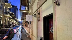 Una calle estrecha con edificios a ambos lados, un letrero que dice 'RUNO inn guest house', y coches estacionados a lo largo de la calle.