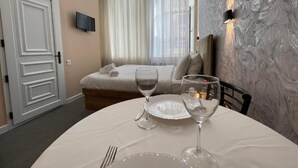 Habitación de hotel con una mesa de comedor preparada para dos, una cama con vistas y un televisor en la pared.
