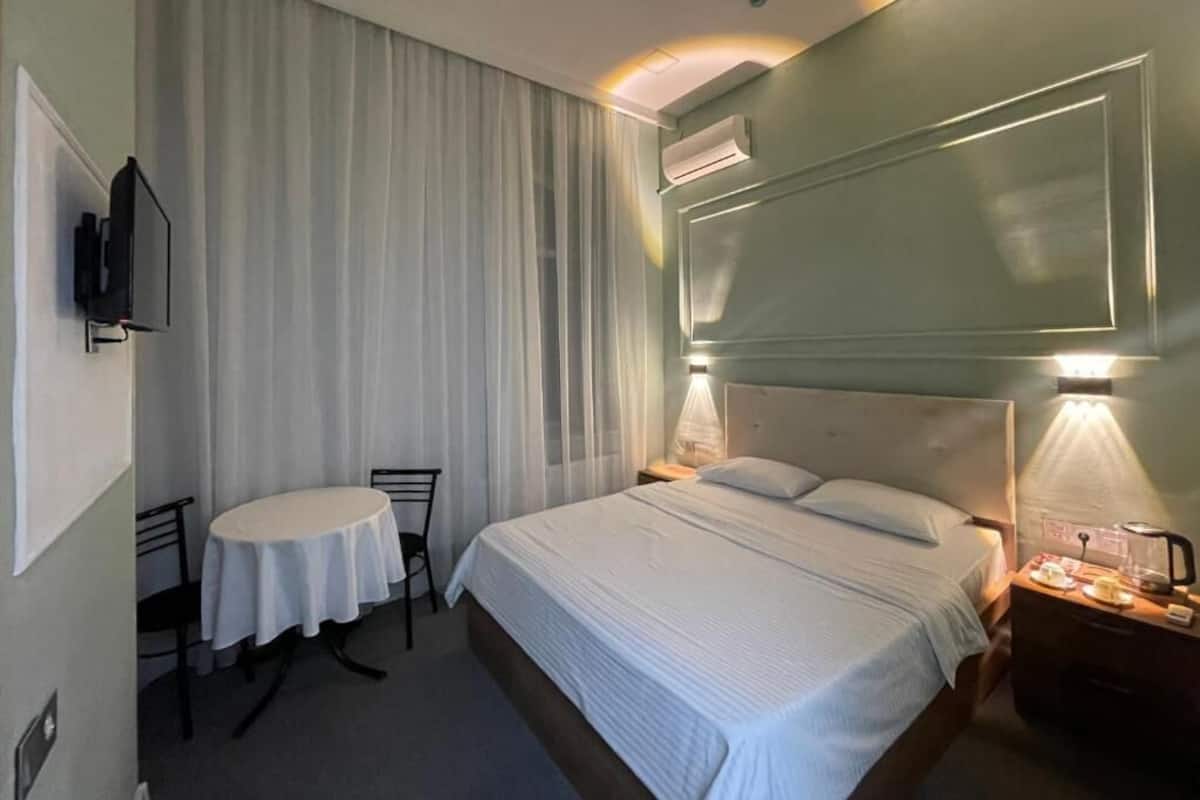 A hotel room with a bed, bedside table, lamp, and a small table with chairs.