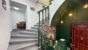 Una escalera con barandillas verdes, un mostrador de recepción y una puerta de madera cerrada con un letrero que dice 'WELCOME'.