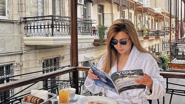 Una persona leyendo un libro en una mesa con comida para el desayuno y vistas al balcón.