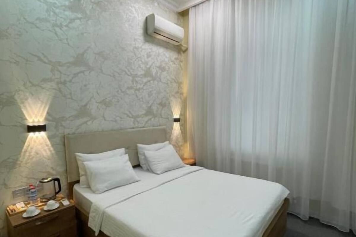 A neatly made bed with white linens, a wooden headboard, and two bedside lamps.