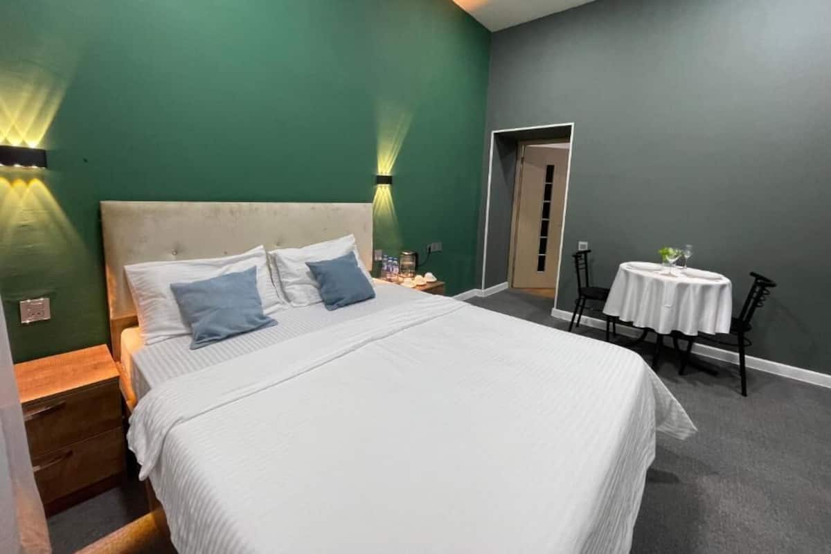 A hotel room with a large bed, bedside tables, a small table with chairs, and a door leading to another room.