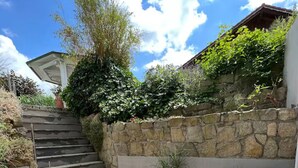 A patio area with a stone wall, a set of stairs, wicker furniture, and potted plants.