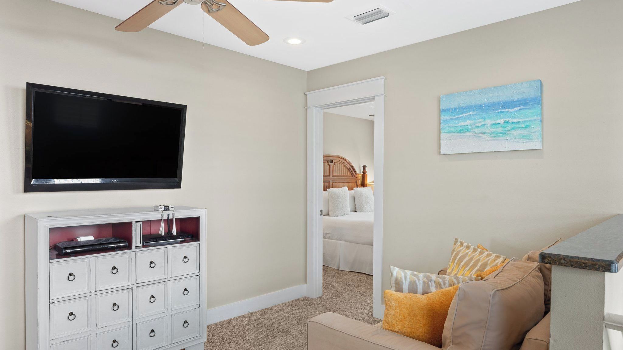 A hotel room with a TV, a white cabinet, a beige sofa, and a painting of a beach scene.