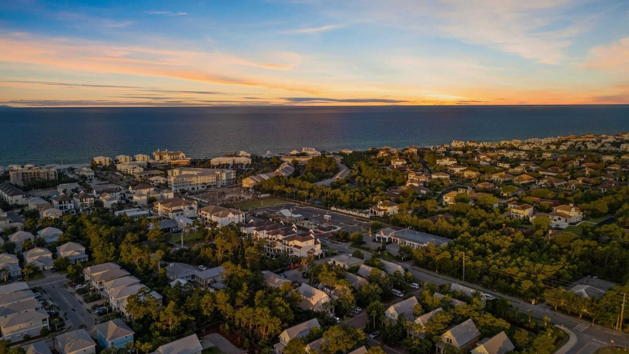 An aerial view of a coastal residential area with houses, roads, and a large body of water.