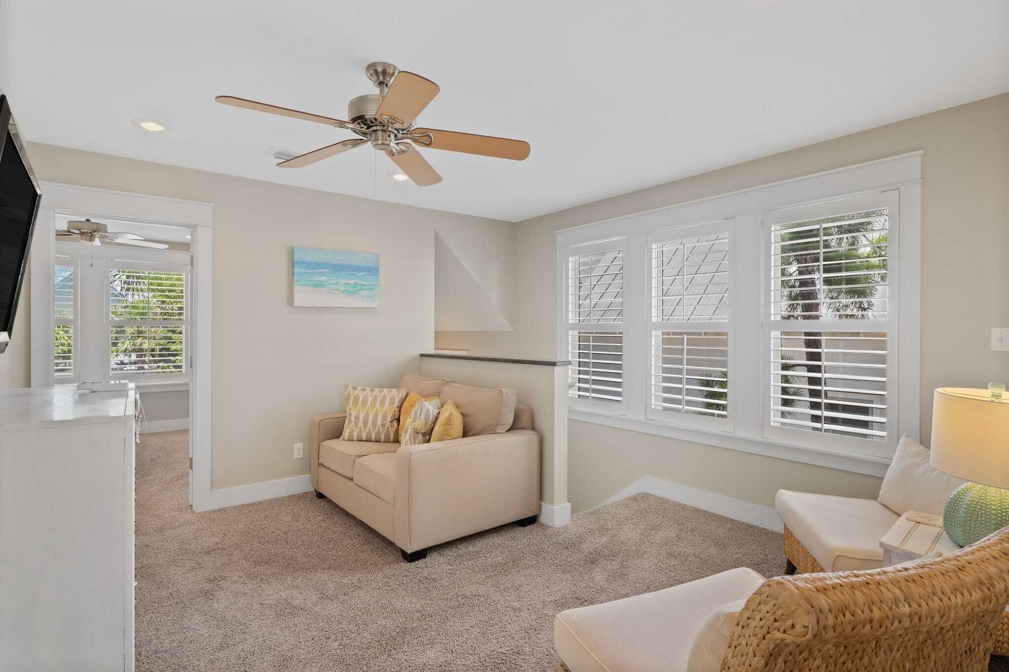 A spacious living room with a beige sofa, a wicker chair, and a ceiling fan.