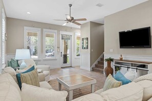 A living room with a ceiling fan, a flat-screen TV mounted on the wall, a coffee table, and a sofa. - Teal Dreams by Avantstay 3 Blocks to Beach, Back Patio Seating (Santa Rosa Beach)