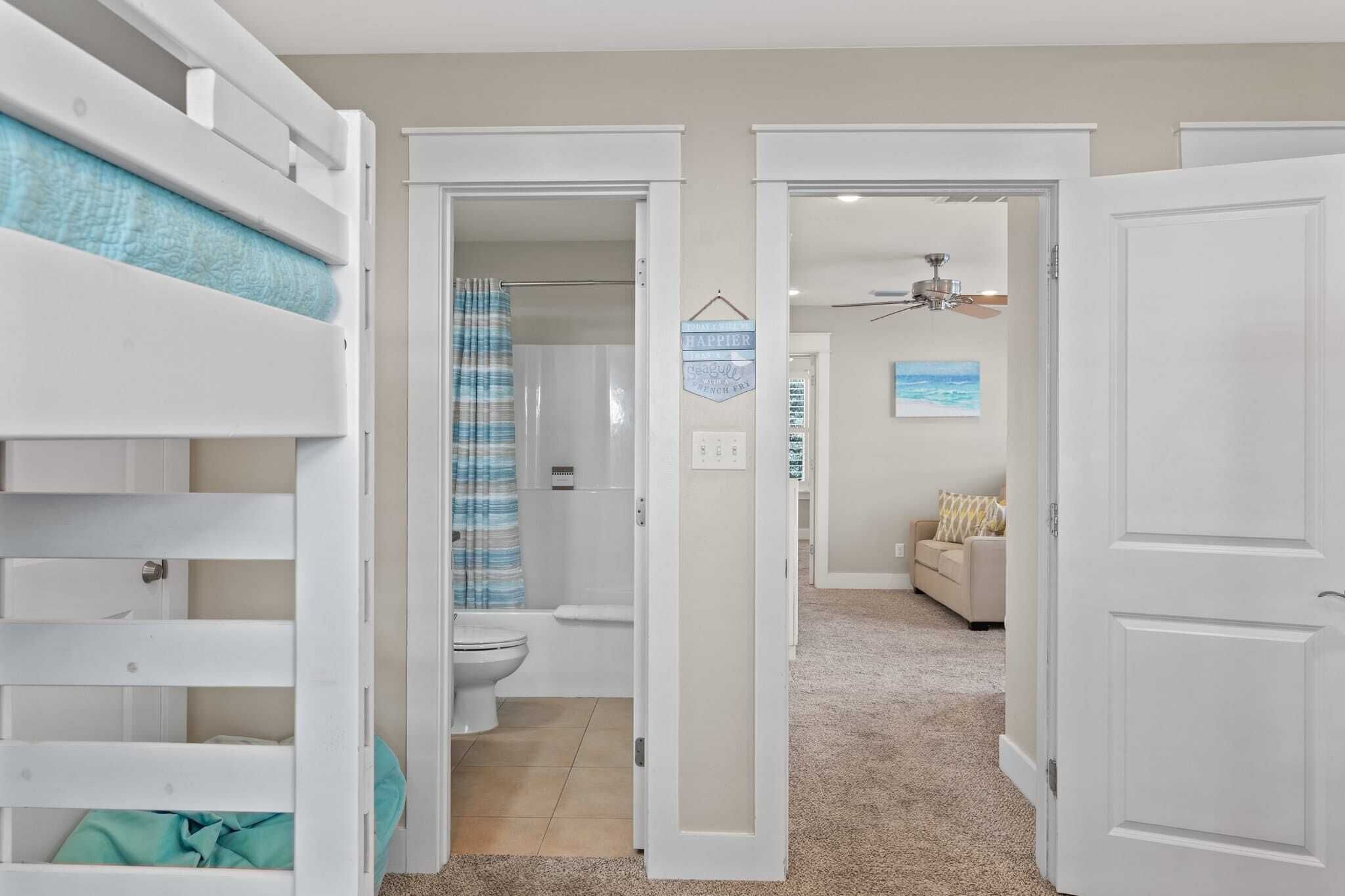 Une chambre avec des lits superposés, une salle de bain avec un rideau de douche et un espace de vie comprenant un canapé et un tableau.