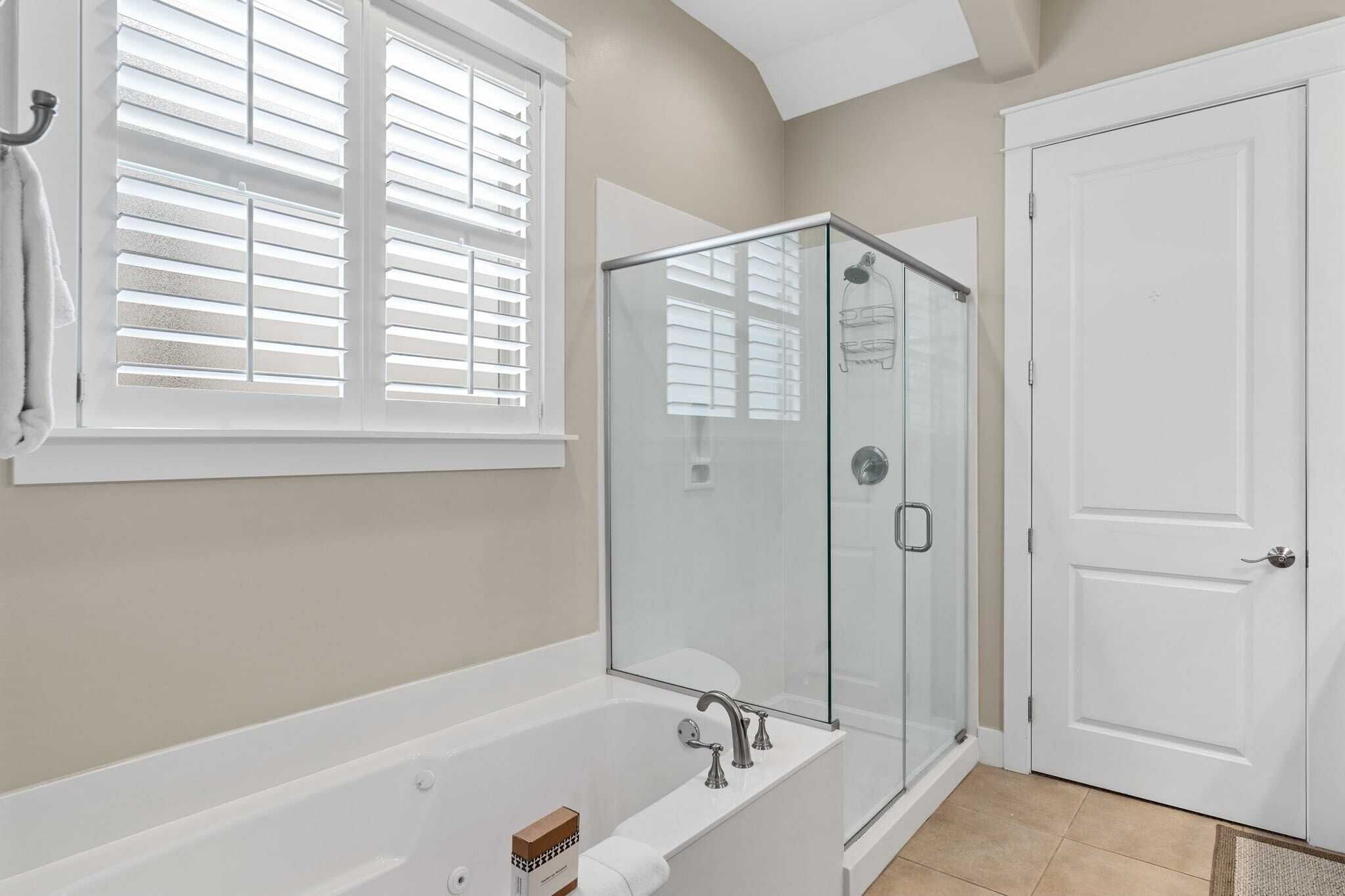 A bathroom with a glass-enclosed shower, a bathtub, and a white door.