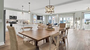 A modern kitchen with white cabinets, a central island, and a dining area with a wooden table and wicker chairs. - This is How We Roll- Shared Pool! (surf City)