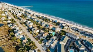 An aerial view of a coastal residential area with houses aligned along the beachfront, a road running parallel to the beach, and a pier extending into the ocean. - This is How We Roll- Shared Pool! (surf City)