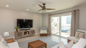 Un salón amplio con una gran televisión de pantalla plana, una mesa de centro de madera, sofás blancos y un balcón con vistas.