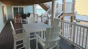 Una terraza de madera con una mesa y sillas, un espacio cubierto y vista a la playa.