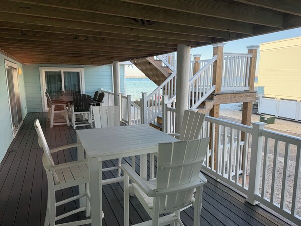 A wooden deck with a table and chairs, a covered area, and a view of the beach.