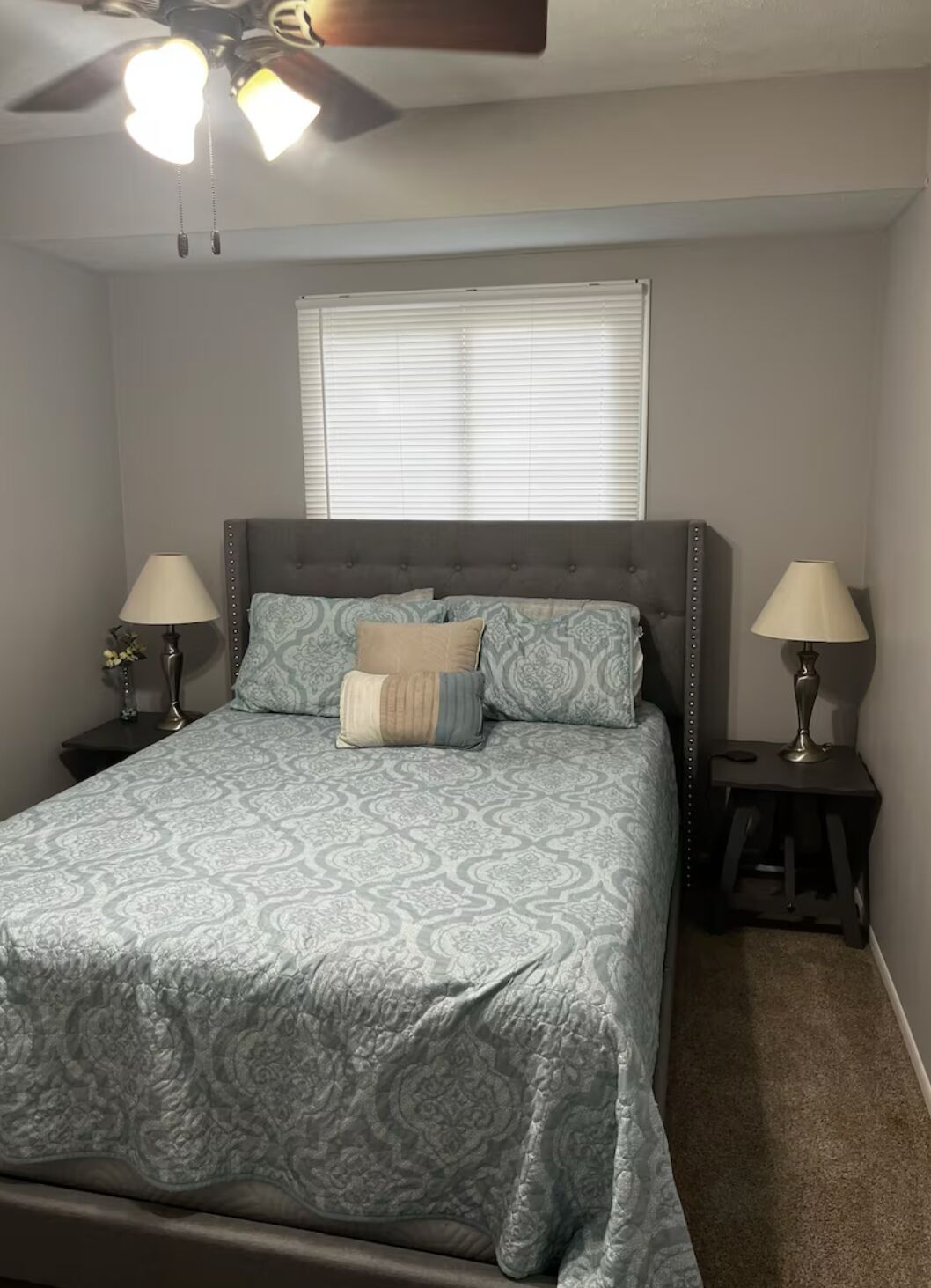 A bedroom with a bed, two bedside tables, a ceiling fan, and a window with blinds.