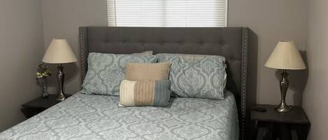 A bedroom with a bed, two bedside tables, a ceiling fan, and a window with blinds.