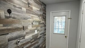 Un couloir avec un mur en bois, une porte dotée d’une fenêtre et un paillasson.