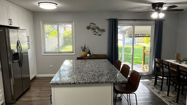 Une cuisine moderne dotée d’un îlot en granit, de meubles blancs et d’un réfrigérateur en acier inoxydable.