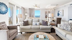 A spacious living room with a large sofa, a coffee table, and a view of the ocean through large windows. - 4 BR Top Floor Beachfront Condo | Beach Club B2010 (Baldwin County)