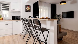 A modern kitchen with white cabinets, a microwave, a coffee machine, and a bar area with chairs. - Stylish City Living Modern Apartment in the hear of Bucharest (București)