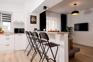 Een moderne keuken met witte kastjes, een magnetron, een koffieapparaat en een bar met stoelen.