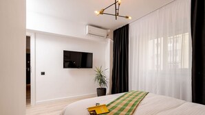 A modern hotel room with a bed, a television, a potted plant, and a window with curtains.