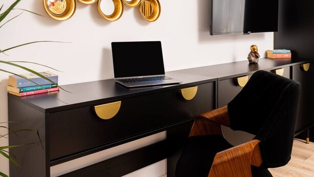 Una habitación moderna con un escritorio negro y dorado, una computadora portátil, una silla y un televisor en la pared.
