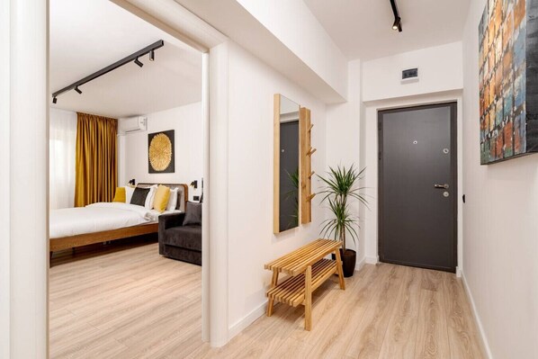 A modern hotel room with a bed, a sofa, a bench, a potted plant, and a door.