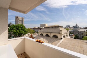 Ein Balkon mit Blick auf ein historisches Gebäude mit Arkaden und einer Kuppel, ein modernes Hochhaus und ein Baum.