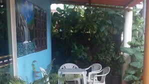 A covered patio area with a mural, white plastic chairs, and potted plants. - Bed and breakfast in a single suite  (Alto Paraíso de Goiás)