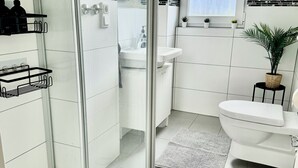 Moderni kylpyhuone, jossa on lasiseinällä varustettu suihku, valkoinen pesuallas ja wc.