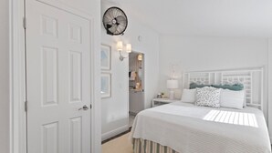 A white bedroom with a bed, bedside lamps, a wall-mounted fan, and a door. - Anchor Inn 02 | 1BR/1BA Boca Grande, Chic Comfort (Boca Grande)
