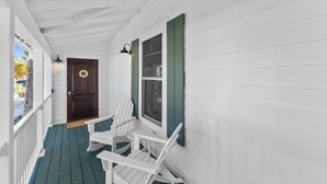 A white porch with a dark door, white chairs, and a window with green shutters. - Anchor Inn 02 | 1BR/1BA Boca Grande, Chic Comfort (Boca Grande)