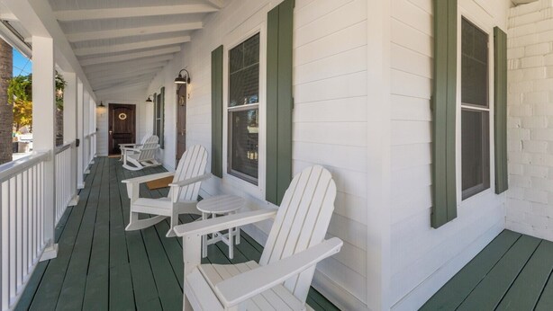 Eine überdachte Veranda mit weißen Adirondack-Stühlen und grünen Fensterläden.