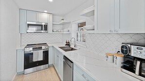 A modern kitchen with white cabinetry, a stainless steel stove, a microwave, and a coffee machine.