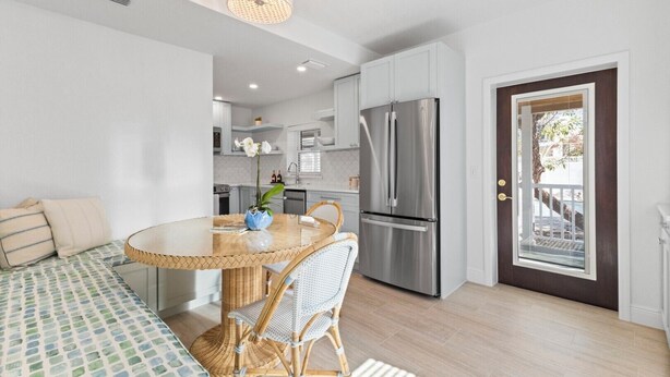 A modern kitchen with white cabinets, a stainless steel refrigerator, and a dining area with a round table and wicker chairs.