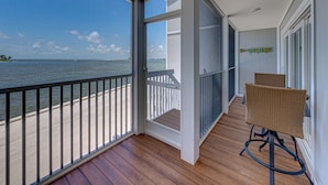 A balcony with a view of the sea, wooden flooring, and wicker chairs.