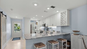 A modern kitchen with white cabinets, a marble island, and a view of the outside.